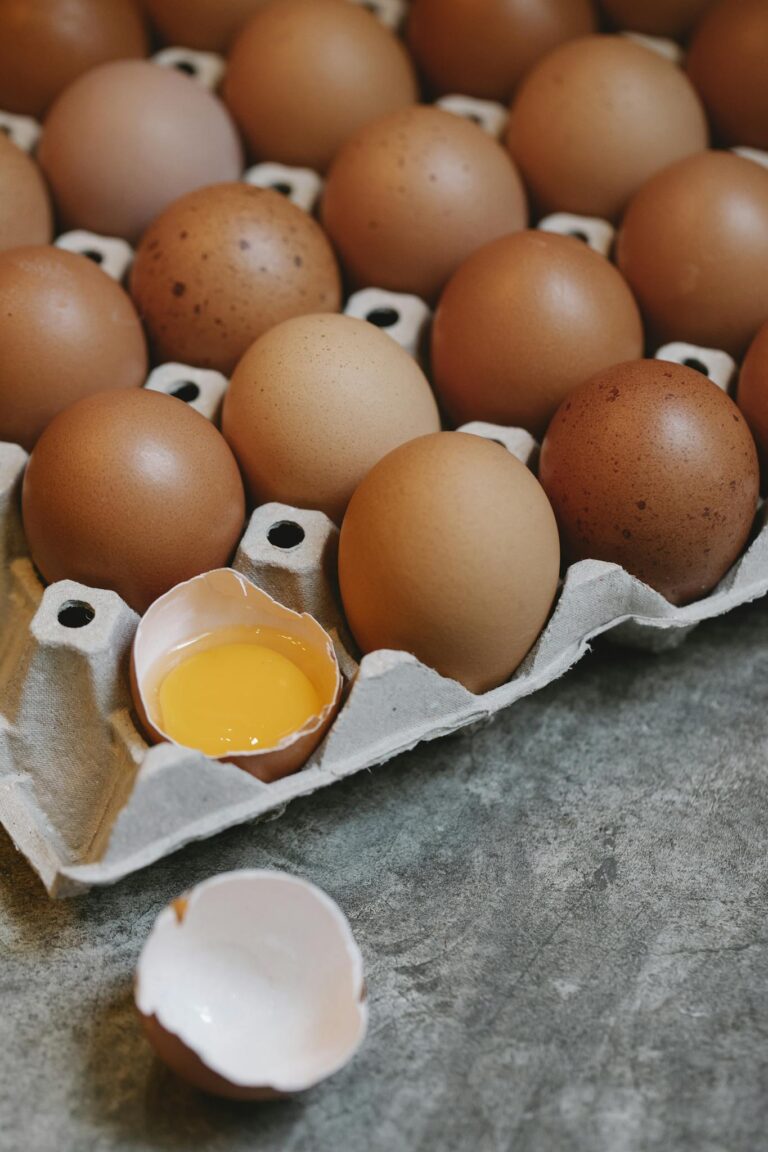 High angle of raw brown chicken eggs placed in recycled carton container on marble table